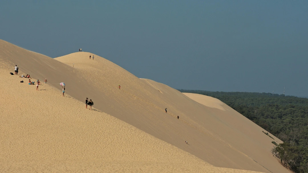 Randonneurs et familles sur les pentes de la Dune du Pilat par temps clair, proche d’Arcachon, une escapade nature idéale en train depuis Bordeaux.